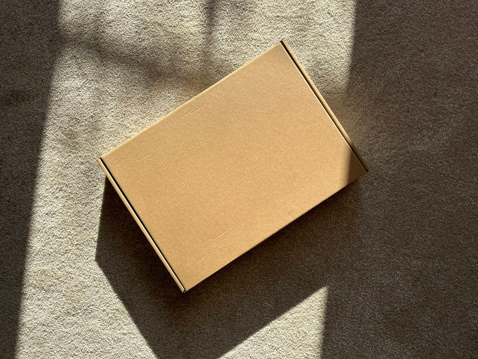 Plain cardboard box on a textured surface in sunlight
